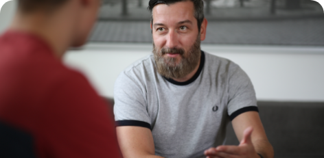 ein Mann mit kurzen braunen Haaren und dunklem, grauen Vollbart sitzt jemandem gegenüber und hört ihm zu. ein Mann mit kurzen braunen Haaren und dunklem, grauen Vollbart sitzt jemandem gegenüber und hört ihm zu.