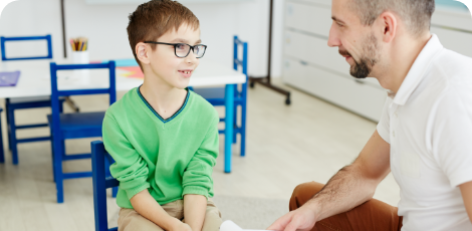 ein kleiner Junge mit kurzen braunen Haaren und dunkler Brille sitzt auf einem Stuhl und hört einem Erwachsenen zu, der ihm gegenüber sitzt ein kleiner Junge mit kurzen braunen Haaren und dunkler Brille sitzt auf einem Stuhl und hört einem Erwachsenen zu, der ihm gegenüber sitzt